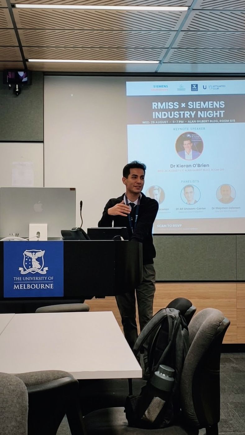 Ramin at a University of Melbourne lectern in front of the Industry Night slide